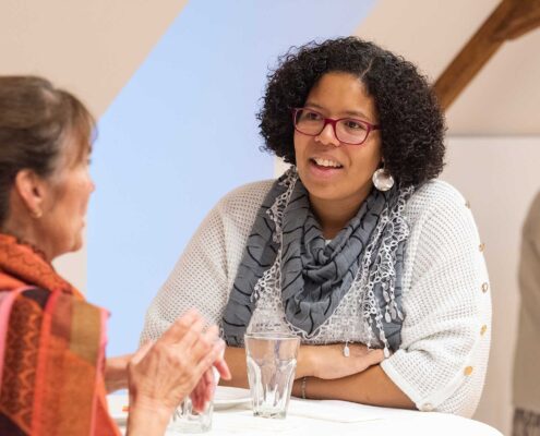 Zwei Personen im Gespräch an einem Stehtisch an der Präsident*innenkonferenz von Agile. Die Szene wirkt wie ein informelles Gespräch bei einer Veranstaltung oder einem Netzwerktreffen.